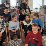Uczniowie siedzą na krzesłach w bibliotece.