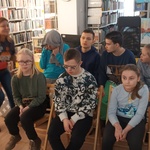 Uczniowie siedzą na krzesłach w bibliotece.
