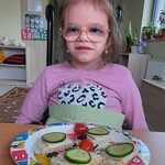 Uczennica trzyma w ręku talerz z samodzielnie wykonanymi kanapkami.