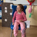 Uczennica siedzi na krześle, uśmiecha się