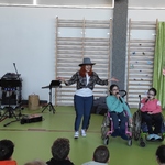Społeczność szkolna ogląda występ uczennic siedzących na wózkach. Obok stoją nauczycielki.