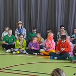 Grupa uczniów siedzi na podłodze i gra na instrumentach.