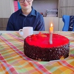 Uczeń siedzi przy stole, na którym stoi tort z cyfrą 16
