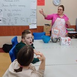 Nauczycielka stoi przy stole na którym leżą składniki spożywcze.