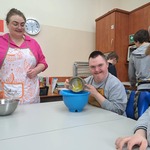 Uczeń przelewa jajka z małej miski do dużej. Obok stoi nauczycielka.