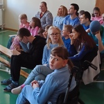 Grupa uczniów siedzi na ławeczkach.