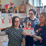 Grupa uczniów stoi wokół opiekunki trzymającej tort.