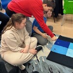 Uczeń kładzie na niebieskim materiale swojego ludzika Lego