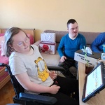 Dziewczyna na wózku. Z tyłu na kanapie siedzi kolega.