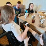 Uczniowie siedzący na kanapie za stołem patrzą na Natalkę oglądającą zdjęcie wyświetlane na ekranie telefonu.