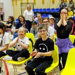 Uczniowie siedzą na żółtych krzesłach.