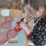 Uczennica kroi paprykę. Przed nią leżą na stole kanapki z salami.