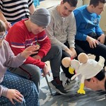 Uczennica rzucę specjalną, orzepowaną piłkę w czapkę w kształcie kury nałożoną na głowę nauczyciela