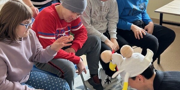 Uczennica rzucę specjalną, orzepowaną piłkę w czapkę w kształcie kury nałożoną na głowę nauczyciela