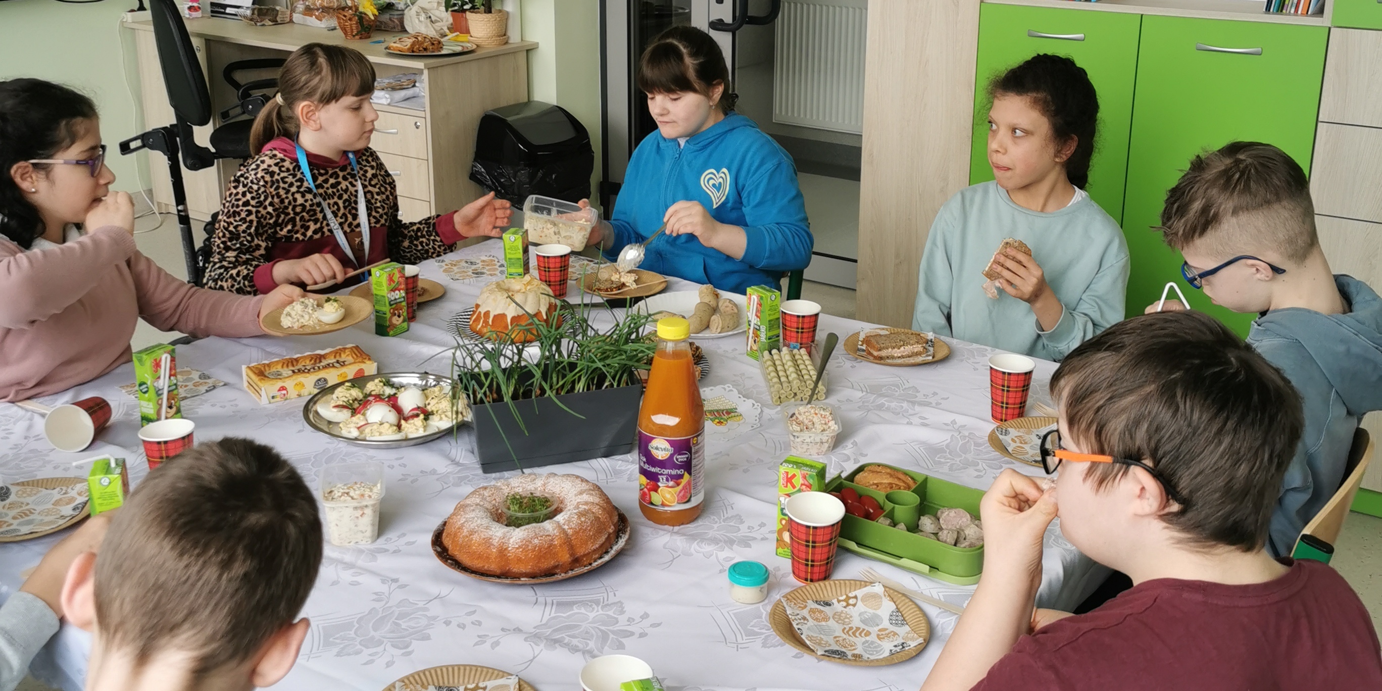 Uczniowie siedzą wokół stołu i jedzą świąteczne śniadanie