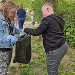 Uczniowie w niebieskich rękawiczkach podczas sprzątania świata, zbierają śmieci i wrzucają do worka