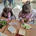 Uczennice siedzą przy stolikach i kroją warzywa