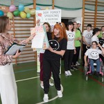 Pani Beata odbiera podziękowania z rąk organizatora imprezy. Z tyłu stoją uczniowie szkoły