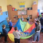 Grupa uczniów i nauczycielka stoją w kole i trzymają chustę animacyjną