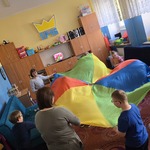 Grupa uczniów i nauczycielka stoją w kole i trzymają chustę animacyjną