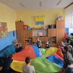 Grupa uczniów i nauczycielki stoją w kole i trzymają chustę animacyjną