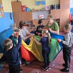 Grupa uczniów i nauczycielki stoją w kole i trzymają chustę animacyjną