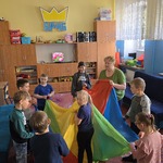 Grupa uczniów i nauczycielka stoją w kole i trzymają chustę animacyjną