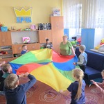 Grupa uczniów i nauczycielka stoją w kole i trzymają chustę animacyjną