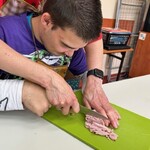 Uczeń z pomocą nauczyciela kroi wędlinę