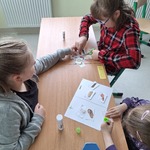 Uczennice siedzą przy stoliku. Wycinają obrazki i wklejaj je do zeszytu.