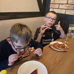 Uczniowie siedzą przy stole i jedzą pizzę