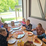 Grupa uczniów siedzi wokół stołu i je pizzę
