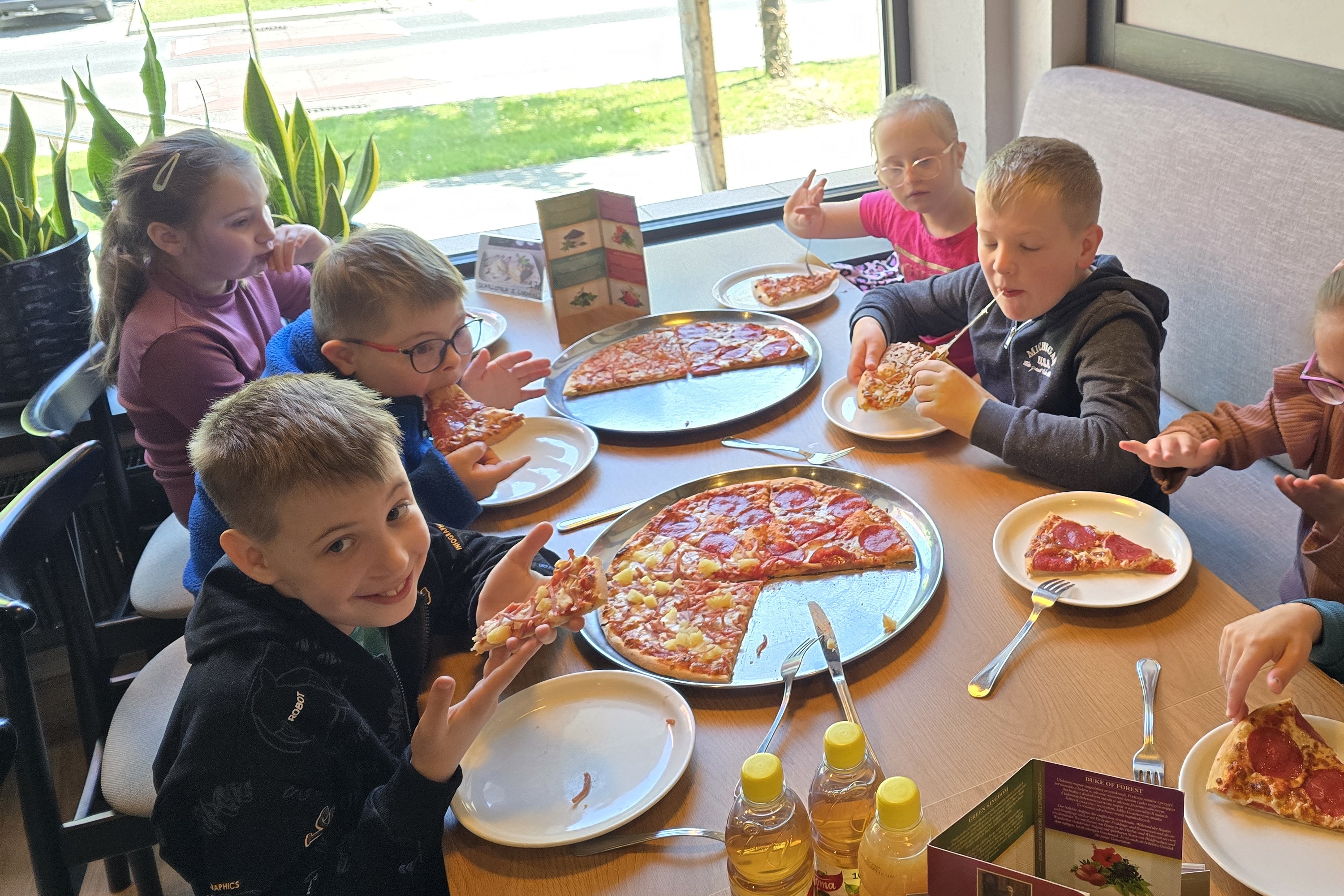 Grupa uczniów siedzi wokół stołu i je pizzę