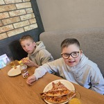 Uczniowie siedzą przy stole i jedzą pizzę