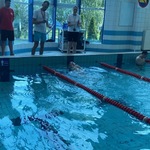 Instruktorzy stoją nad basenem mierząc czas zawodnikowi płynącemu jednym torem