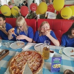 Czwórka uczniów siedzi przy stole i je pizzę