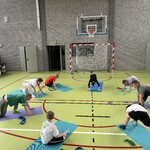 Szkolna sala gimnastyczna. Uczniowie wykonują ćwiczenia na matach