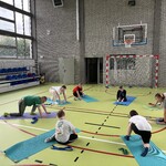 Szkolna sala gimnastyczna. Uczniowie wykonują ćwiczenia na matach