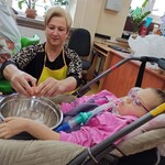Uczennica siedzi na wózku, nauczycielka rozbija jajko do miski