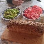 Na stole leży chleb oraz stoją talerze z ogórkami i pomidorami