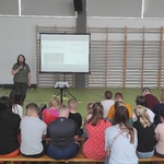 Uczniowie siedzą na ławeczkach i słuchają pani edukator