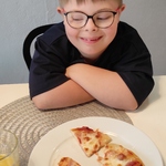 Chłopiec siedzi przy stole. przed nim stoi talerz z pizzą