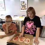 Dziewczyna i chłopiec stoją przy stole. Przed nim blacha z pizzami