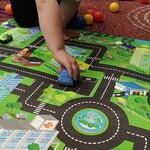 Chłopiec jeździ samochodzikiem po makiecie z ulicami