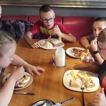 Grupa uczestników półkolonii siedzi przy stoliku w kawiarni i je gofry