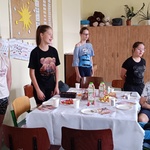 Jubilat siedzi przy urodzinowym stole wokół którego stoją koleżanki