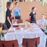 Jubilat siedzi przy urodzinowym stole wokół którego stoją koleżanki