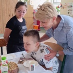Jubilat zdmuchuje świeczkę na torcie. Z tyłu   stoi nauczycielka