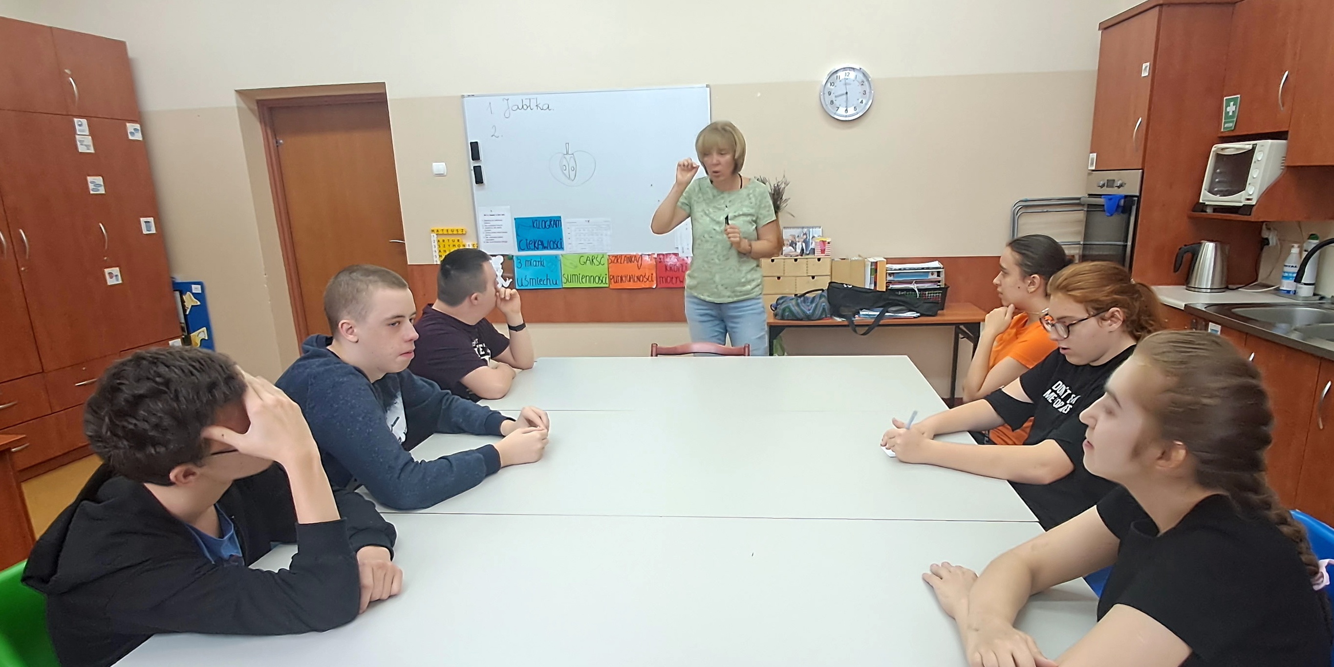 Nauczycielka mówi do uczniów siedzących wokół stołu