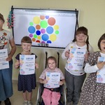 Uczennice z dyplomami na tle tablicy interaktywne z wyświetlonym obrazem kolorowych kropek